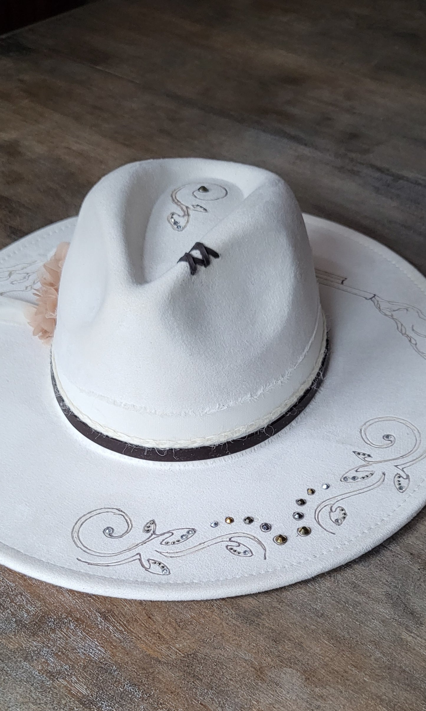 Introducing Miss "Dolly" she is a vegan suede ivory fedora.  She is hand burned and finished with rhinestones, genuine leather stitches, and hatband, then topped off with a flower and rhinestones. 
This hat would be perfect for a wedding!