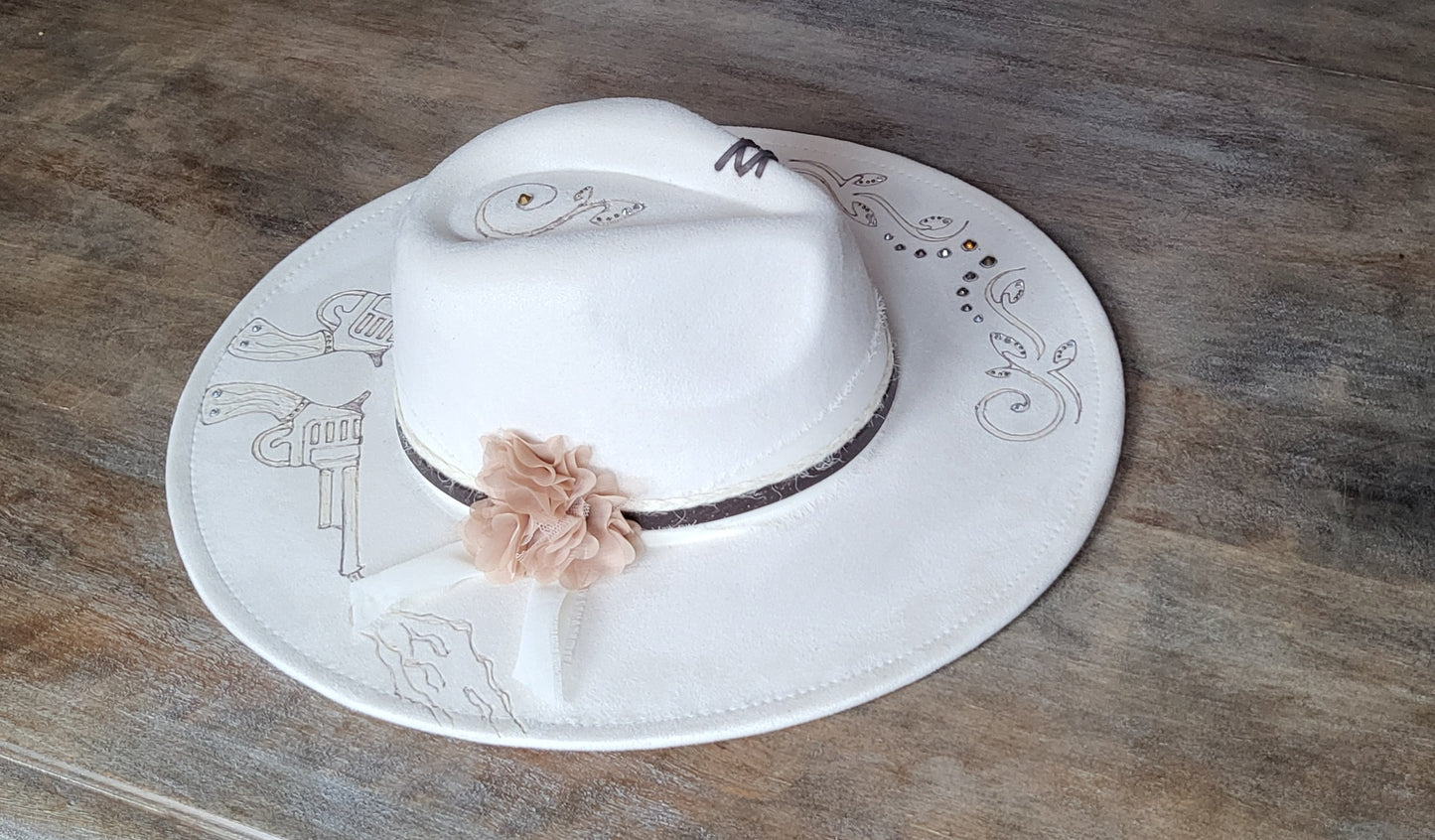 Introducing Miss "Dolly" she is a vegan suede ivory fedora.  She is hand burned and finished with rhinestones, genuine leather stitches, and hatband, then topped off with a flower and rhinestones. 
This hat would be perfect for a wedding!