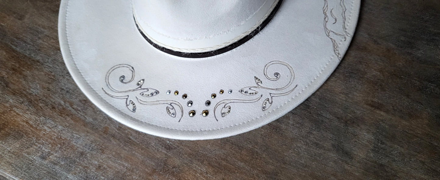 Introducing Miss "Dolly" she is a vegan suede ivory fedora.  She is hand burned and finished with rhinestones, genuine leather stitches, and hatband, then topped off with a flower and rhinestones. 
This hat would be perfect for a wedding!