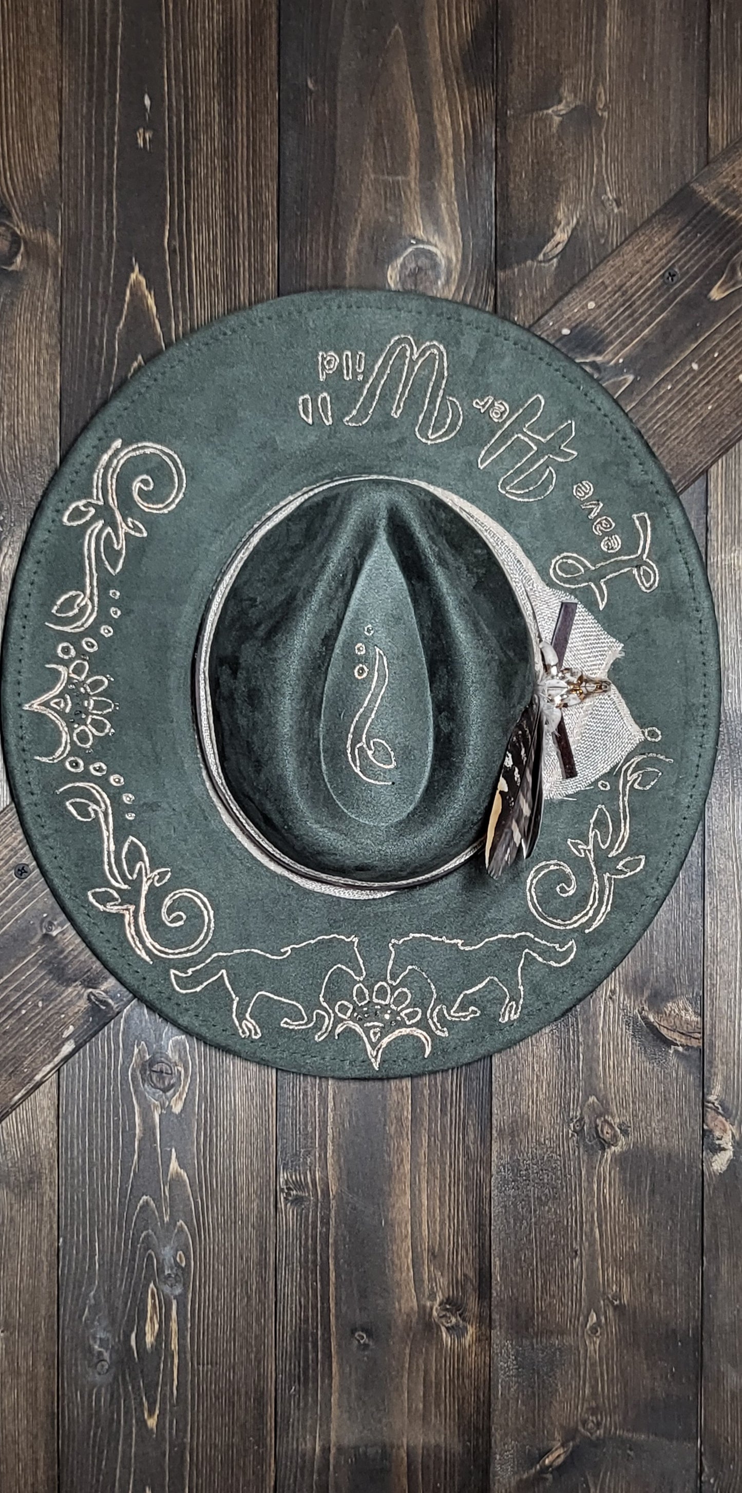 Introducing our "Leave Her Wild" olive green suede fedora cowboy hat that is burned and hand painted in rose gold with rhinestones, burlap, feathers, and genuine leather hatband Embellished with a cowskull