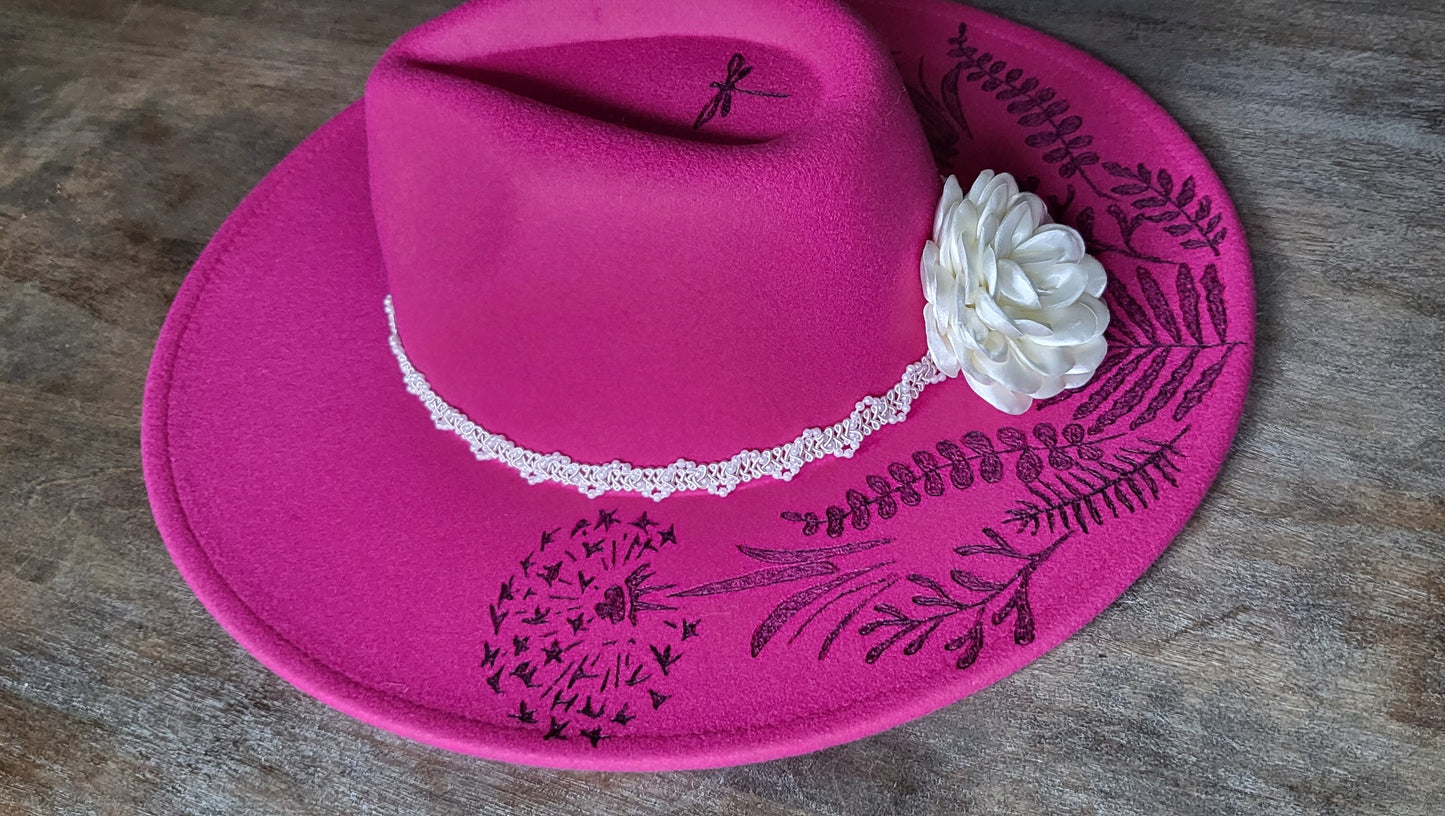 Dandelion wishes. she is hand burned with ferns and dandelions accented with a dragonfly on a raspberry, fully adjustable, vegan felt cowboy fedora hat with a pearl and silk flower hatband