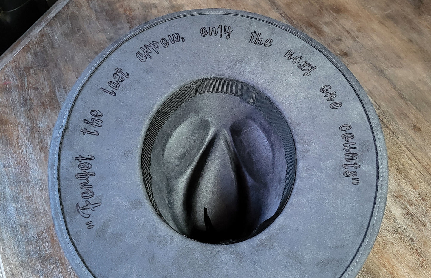 Grey suede burned cowboy hat fedora with the saying "forget the first arrow, only the next one counts"