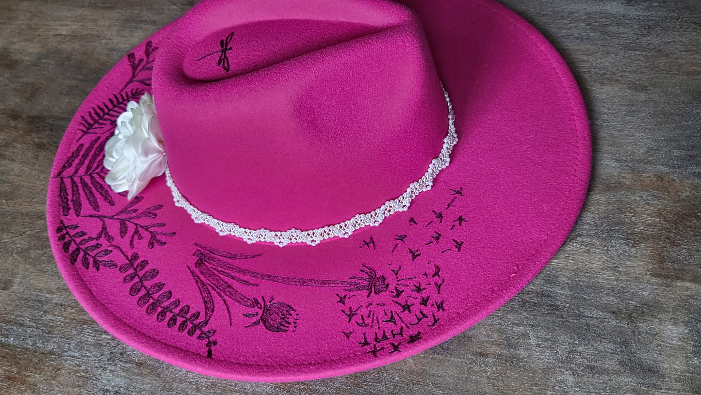 Dandelion wishes. she is hand burned with ferns and dandelions accented with a dragonfly on a raspberry, fully adjustable, vegan felt cowboy fedora hat with a pearl and silk flower hatband