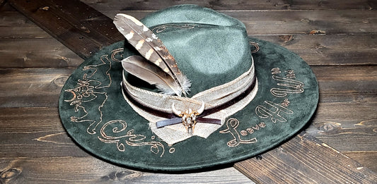 Introducing our "Leave Her Wild" olive green suede fedora cowboy hat that is burned and hand painted in rose gold with rhinestones, burlap, feathers, and genuine leather hatband Embellished with a cowskull