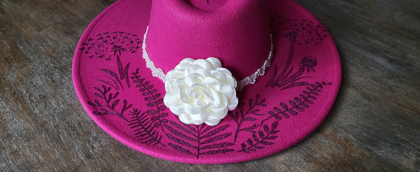 Dandelion wishes. she is hand burned with ferns and dandelions accented with a dragonfly on a raspberry, fully adjustable, vegan felt cowboy fedora hat with a pearl and silk flower hatband