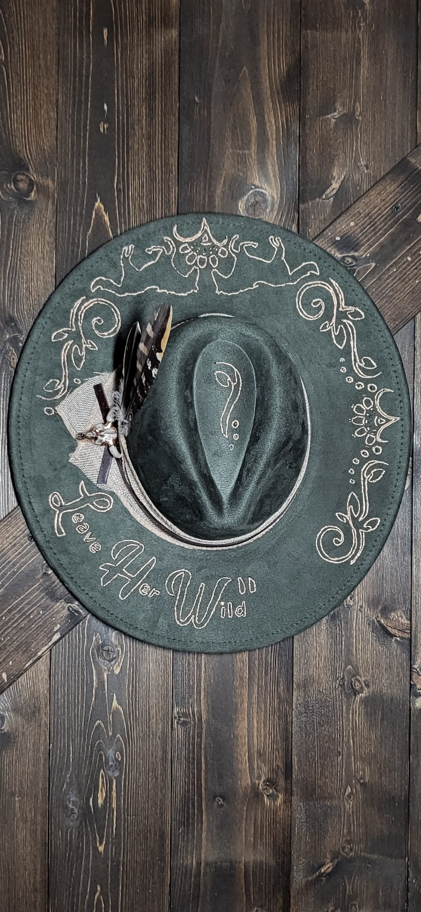 Introducing our "Leave Her Wild" olive green suede fedora cowboy hat that is burned and hand painted in rose gold with rhinestones, burlap, feathers, and genuine leather hatband Embellished with a cowskull