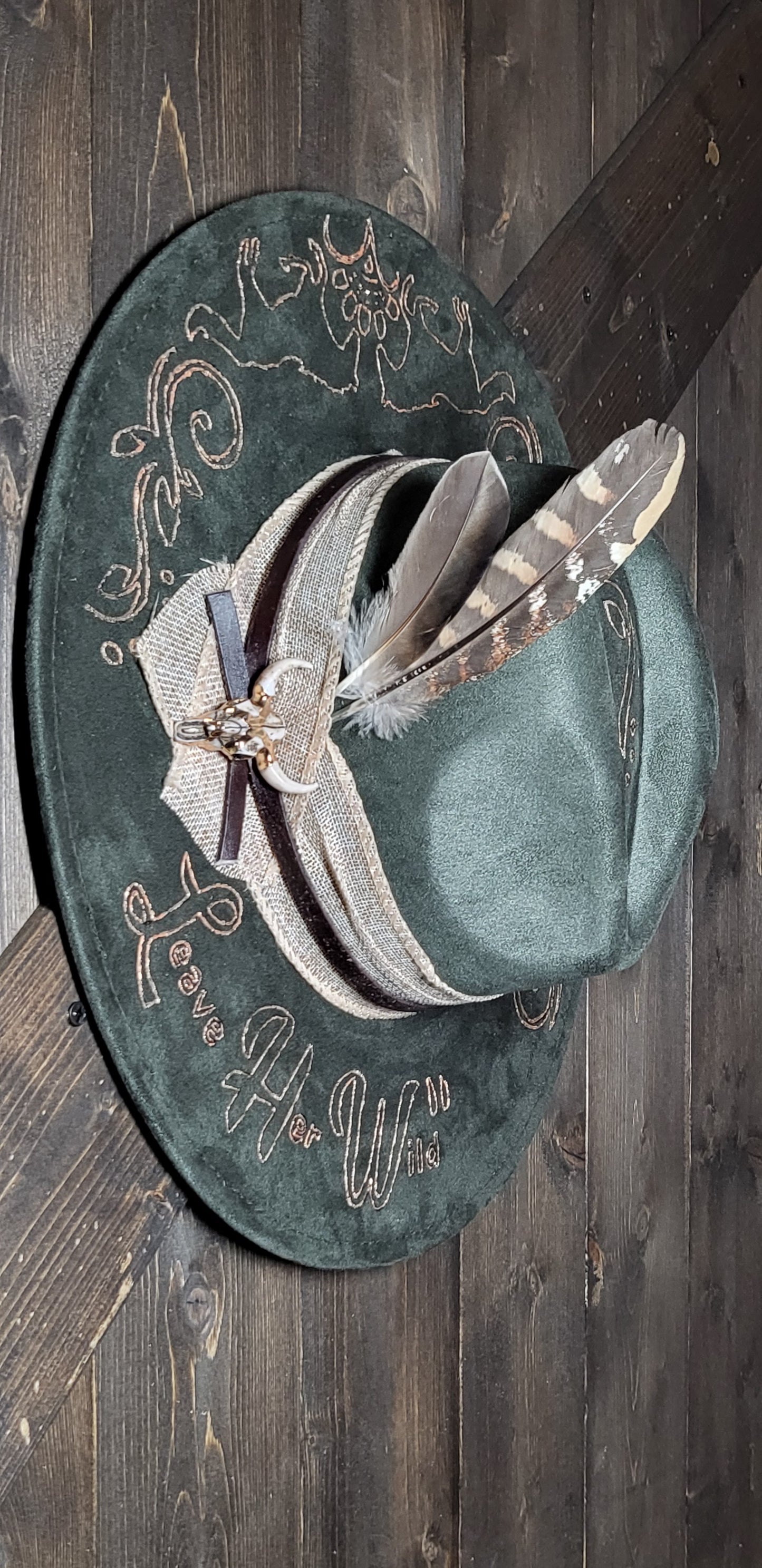 Introducing our "Leave Her Wild" olive green suede fedora cowboy hat that is burned and hand painted in rose gold with rhinestones, burlap, feathers, and genuine leather hatband Embellished with a cowskull